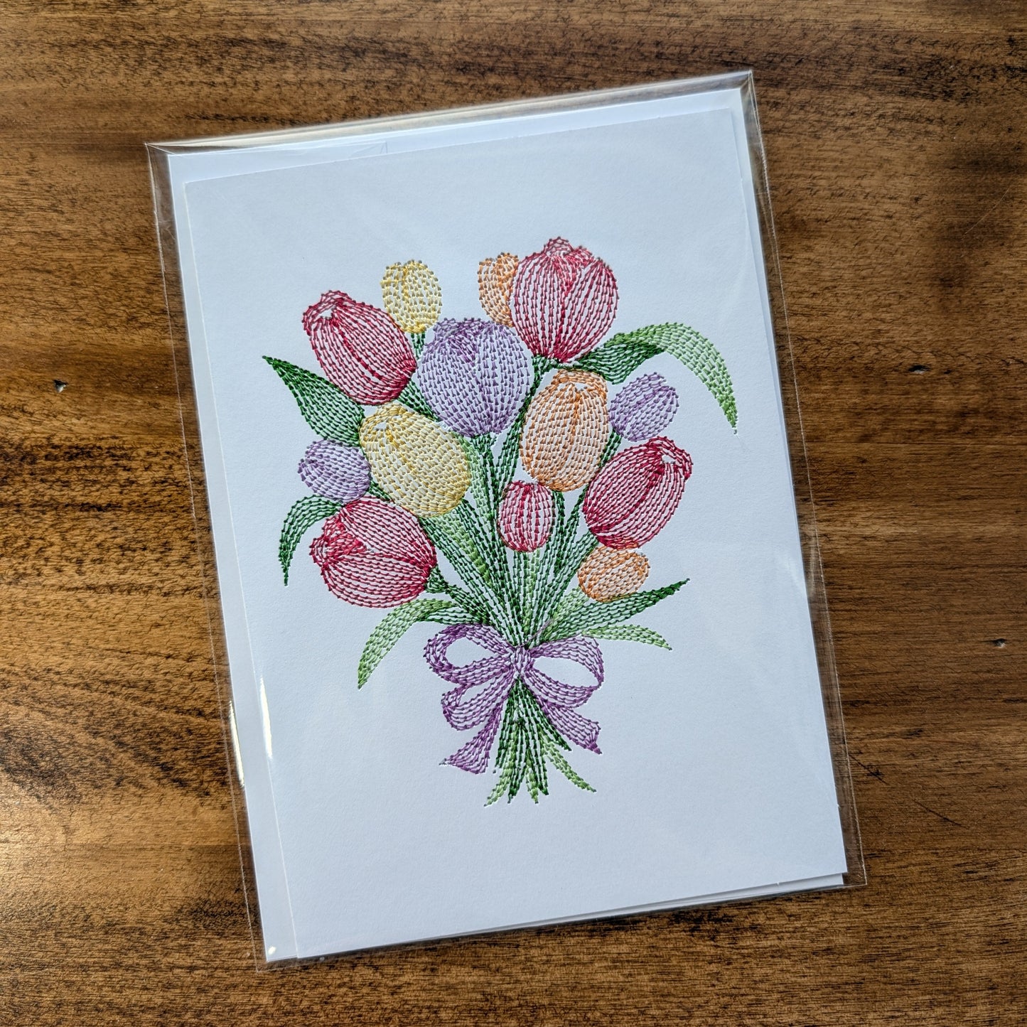 Card with embroidered tulip design on a wooden surface